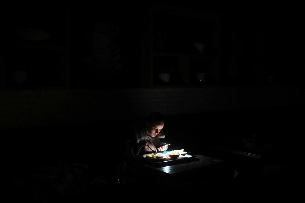 Una ragazza utilizza la torcia del suo smartphone per vedere il cibo nel piatto durante un blackout a Kiev, Ucraina.